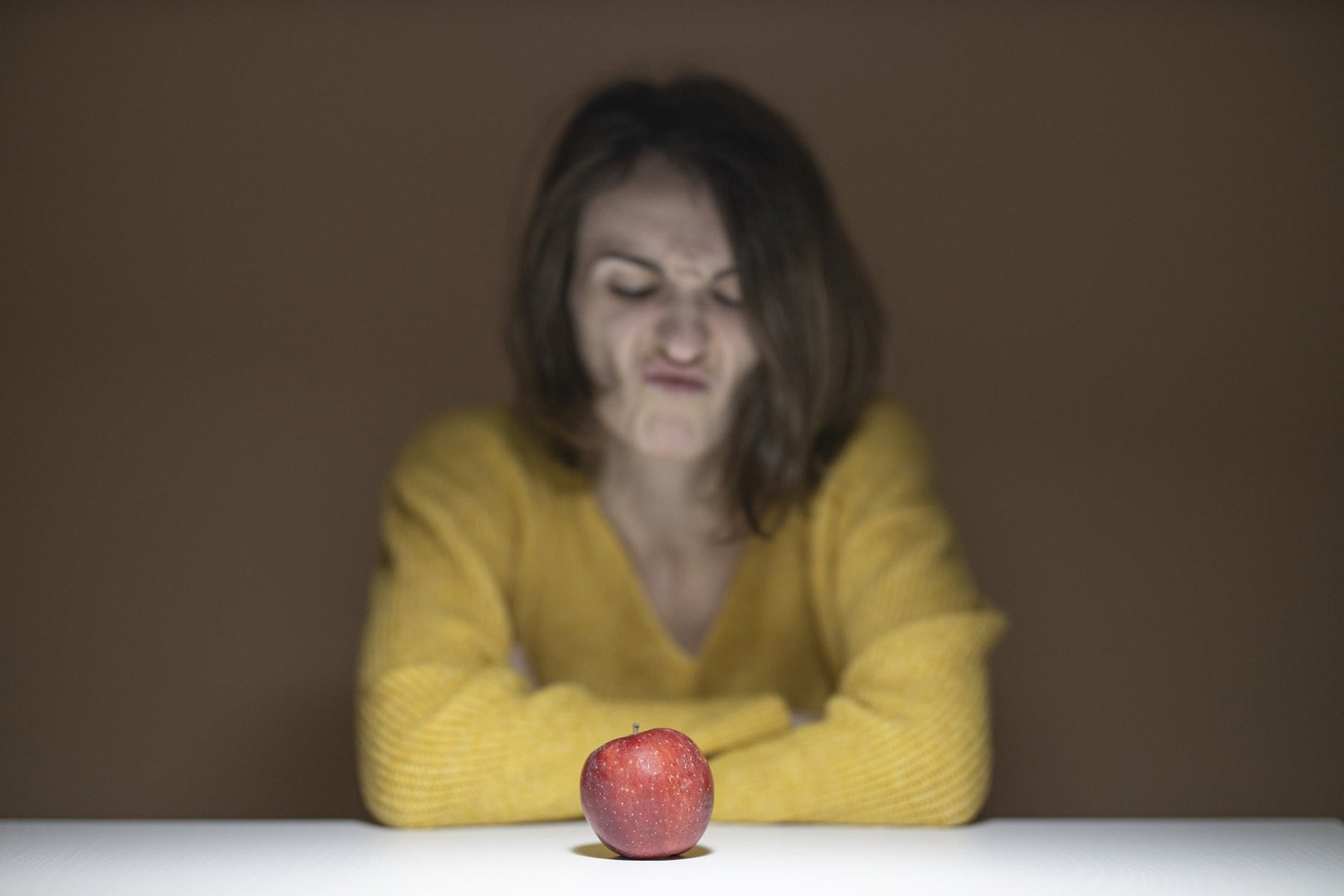 Angry woman looking down a red apple on a table