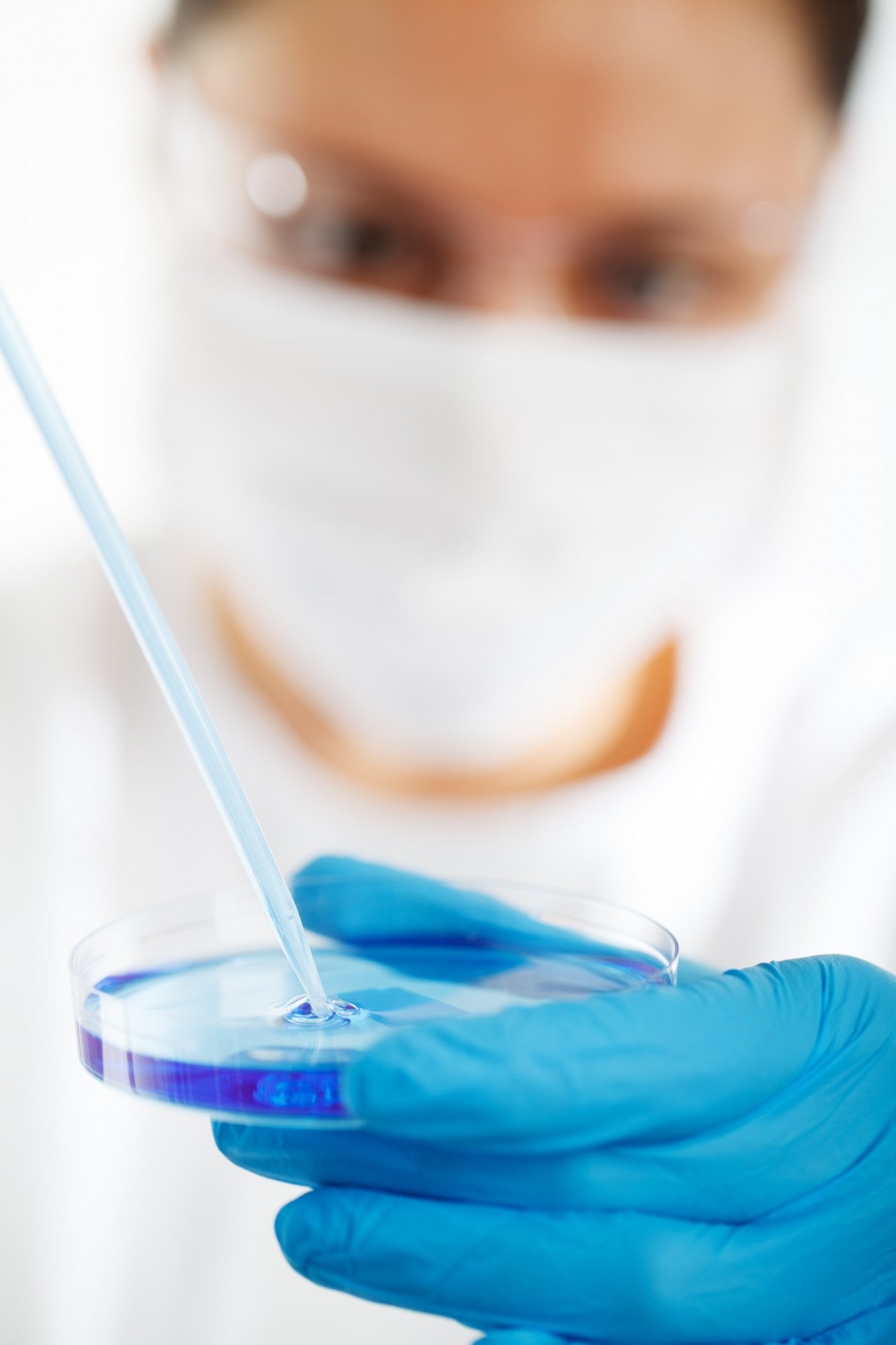 Man out of focus with blue gloves pouring liquid in a recipient
