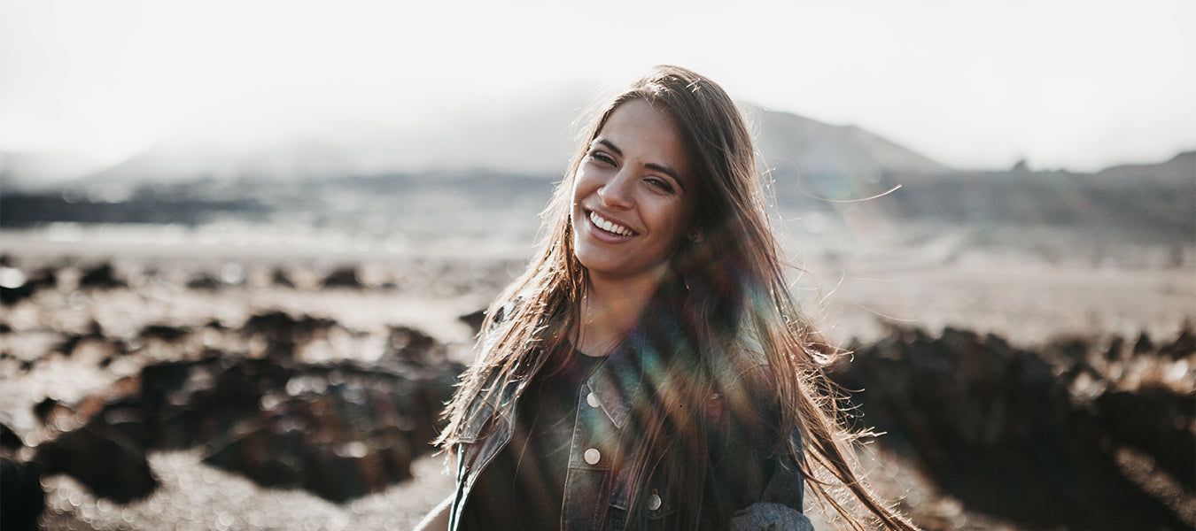 Brunette woman smiling with a mountain and sun behind her