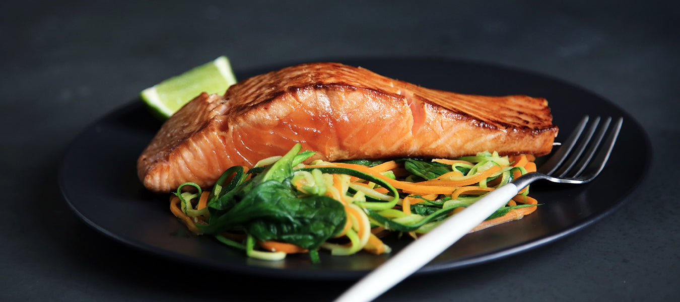 Grilled salmon with greens on a black plate sitting on a black table