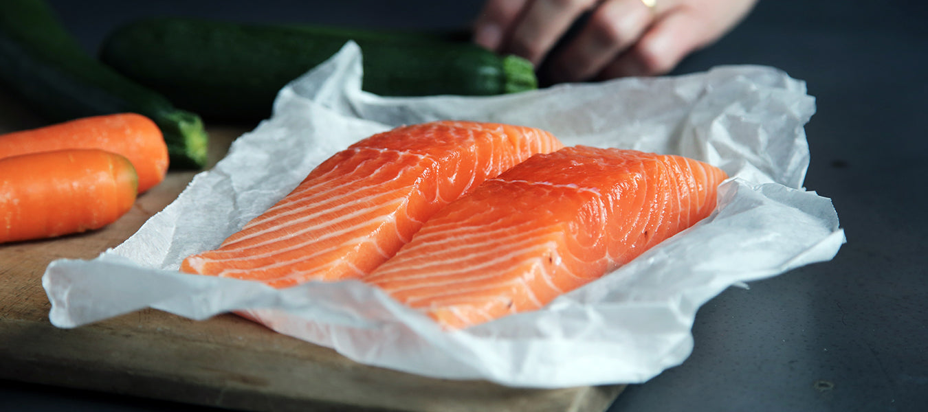 Salmon on a white sheet sitting on a black table with two carrots nearby