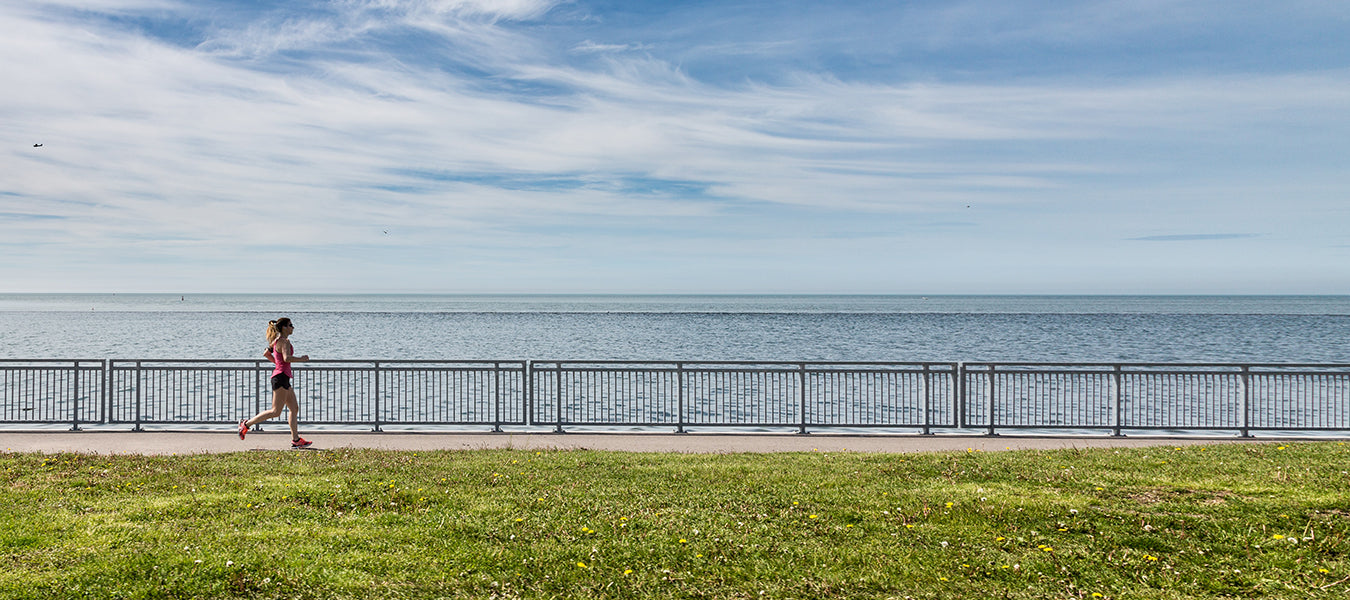 Woman running next to a beach and green field