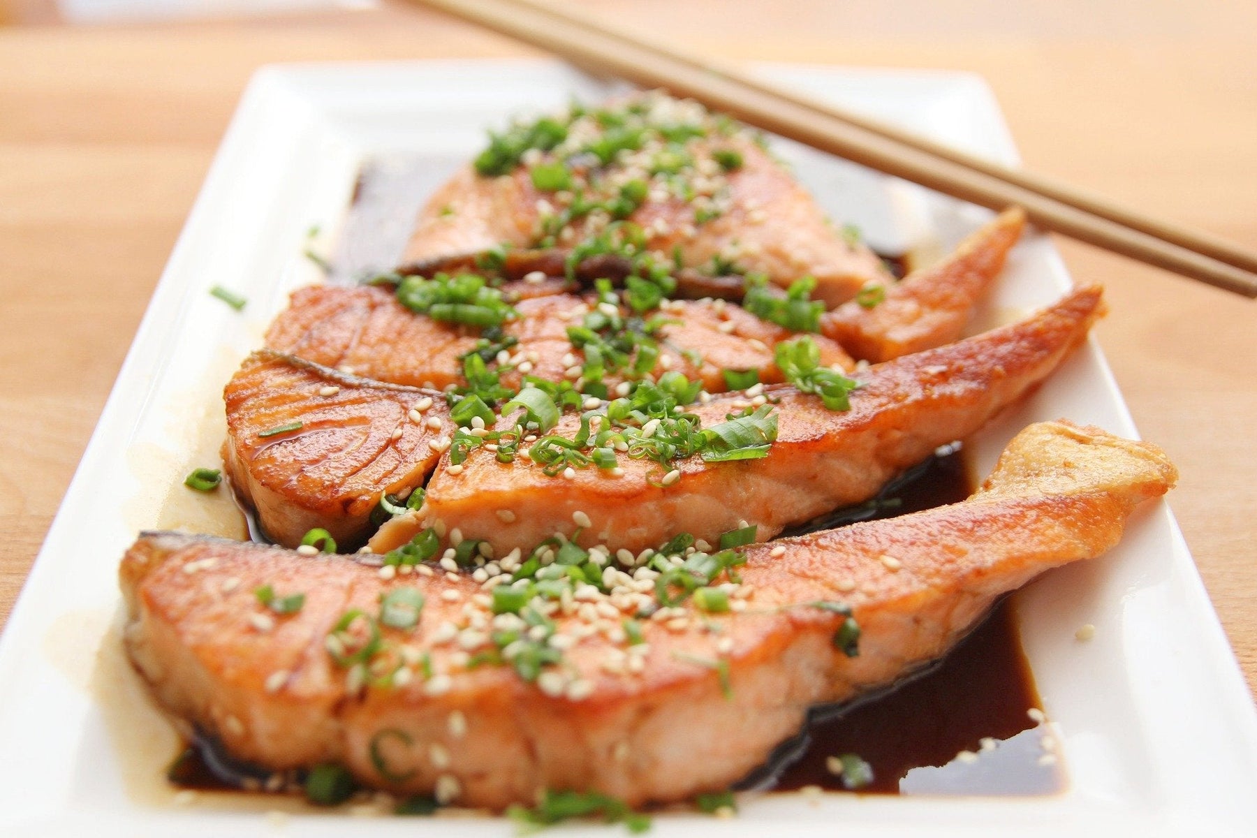 Salmon seasoned with greens sitting on a white plate along with chopsticks