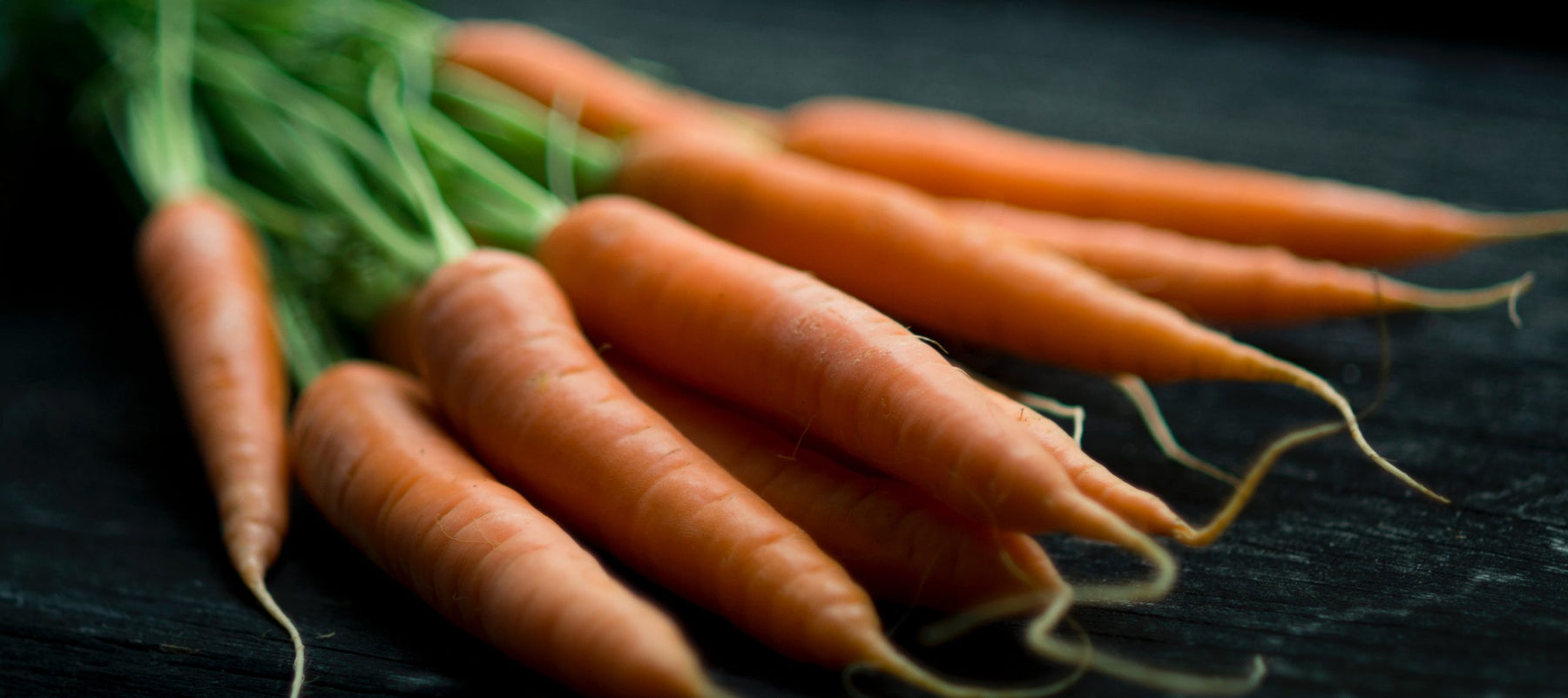A bunch of carrots with leaves sitting on a black table