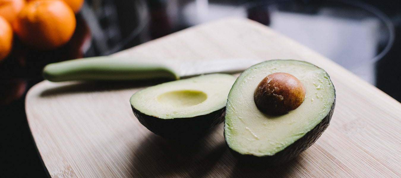 Avocado cut in half on a table along with a knife