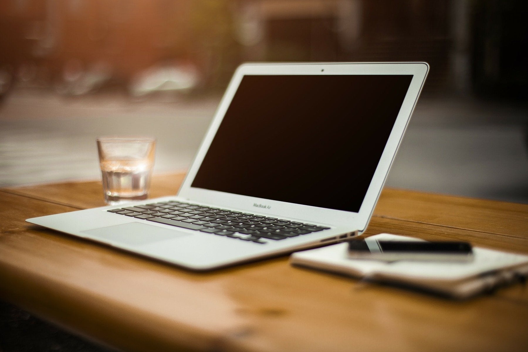 A laptop along with a glass of water and a notebook over a wooden desk