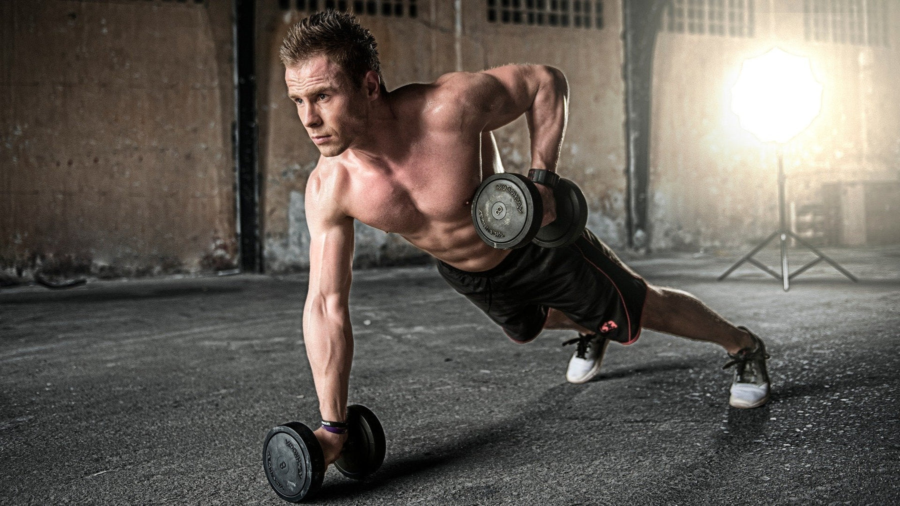 Shirtless man exercises with dumbells from pushup position