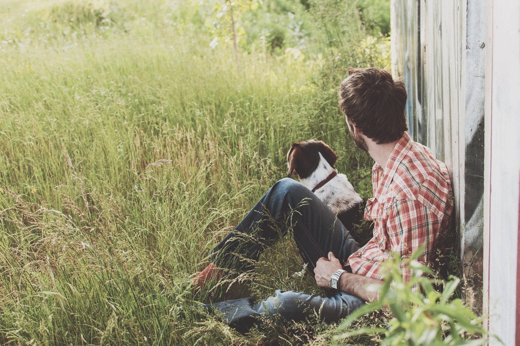 Man and a dog laying on the grass next to a white fence