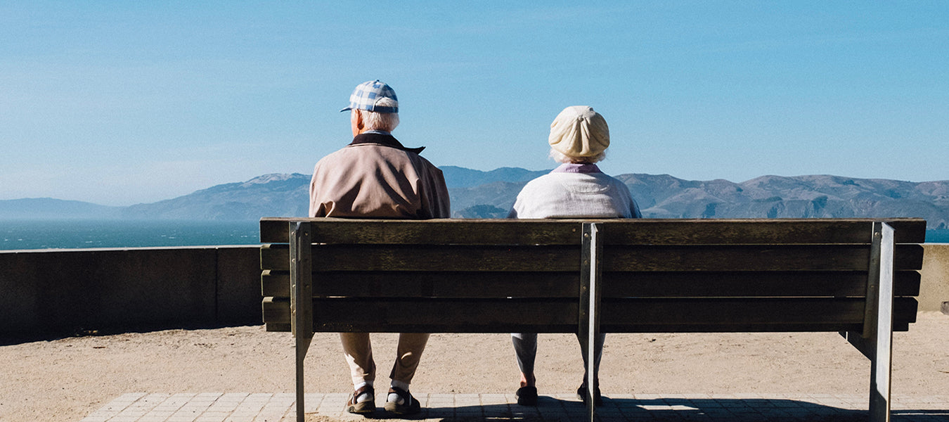 Old woman and old man sitting on a bench watching the mountain