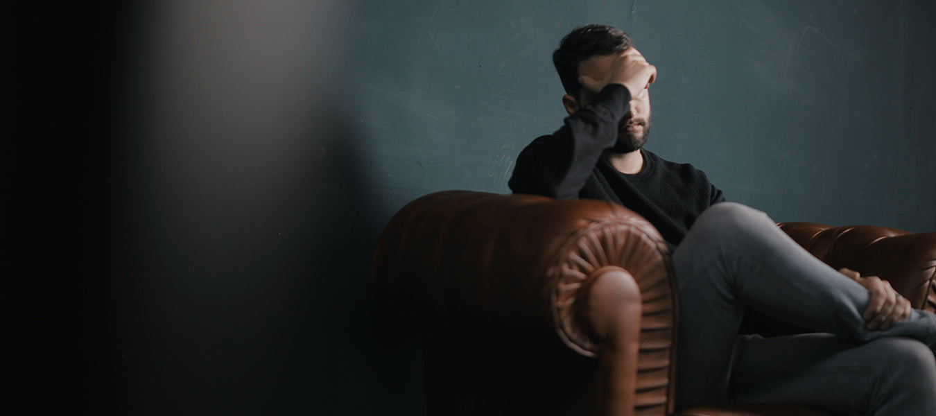 Man with headache laying on a brown lather sofa