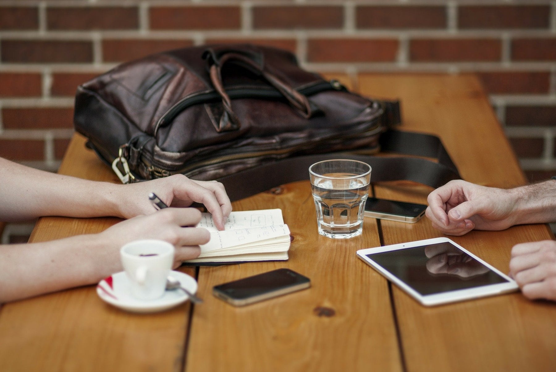 Two women taking notes over a wooden desk with a brown bag on the table