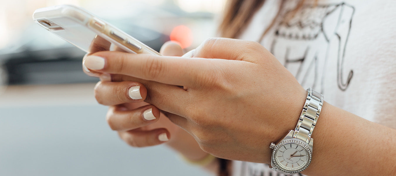 Woman dressed in white with white nails and a watch holding a smartphone