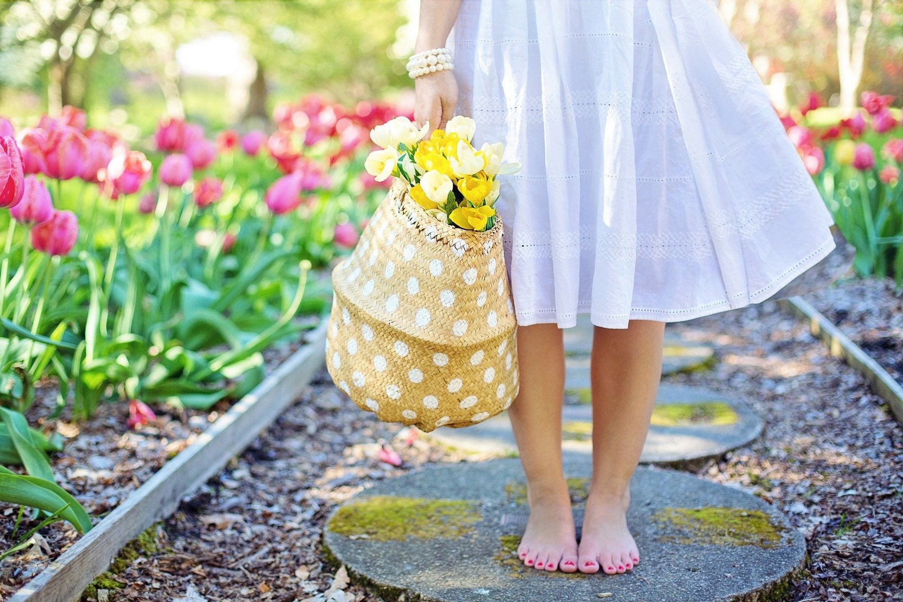 Girl in a white dress sitting on a piece of stone, surrounded by a garden of flowers