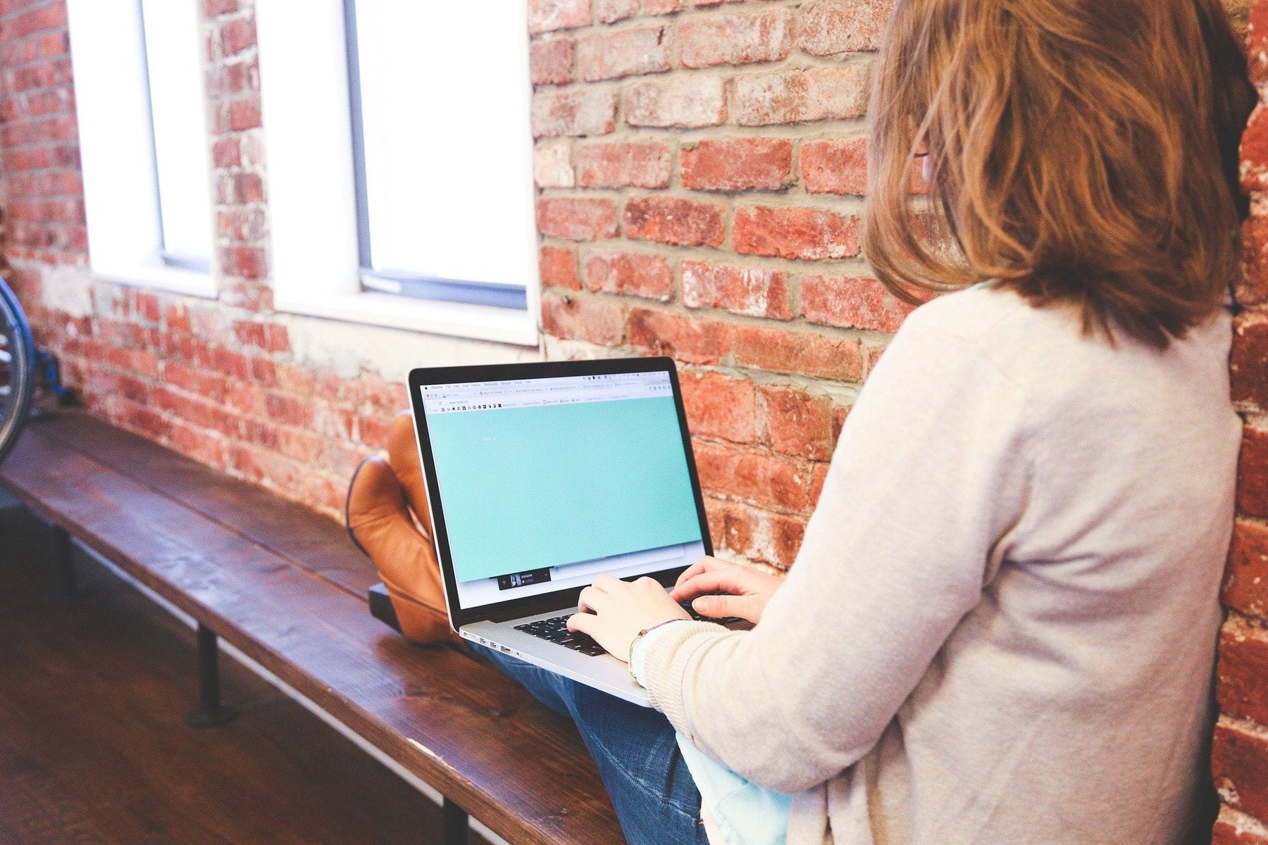Woman sitting on a wooden bench working on a laptop