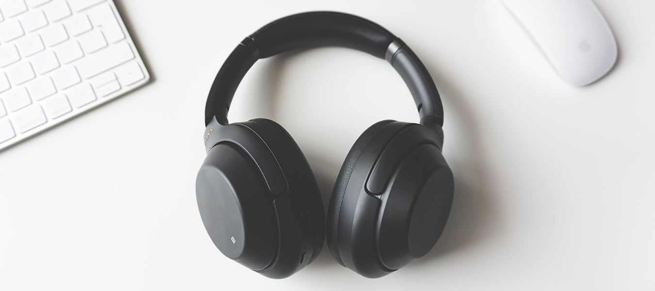 Black headphones on a white table next to a white mouse and keyboard