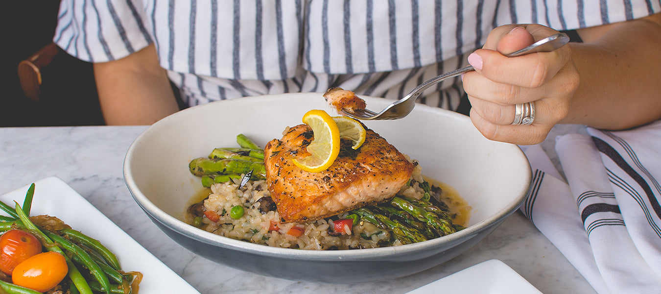 Woman eating salmon with rice and asparagus from a white plate