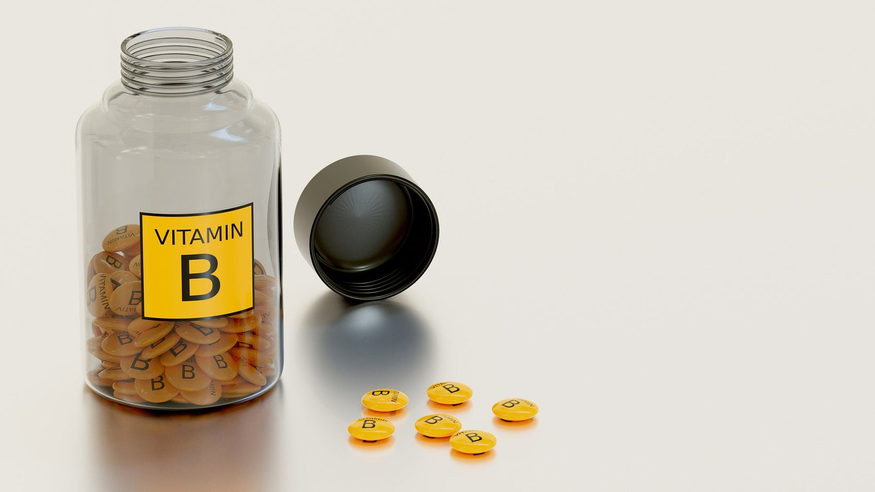 Glass bottle labeled Vitamin B half full with pills along some pills on the table