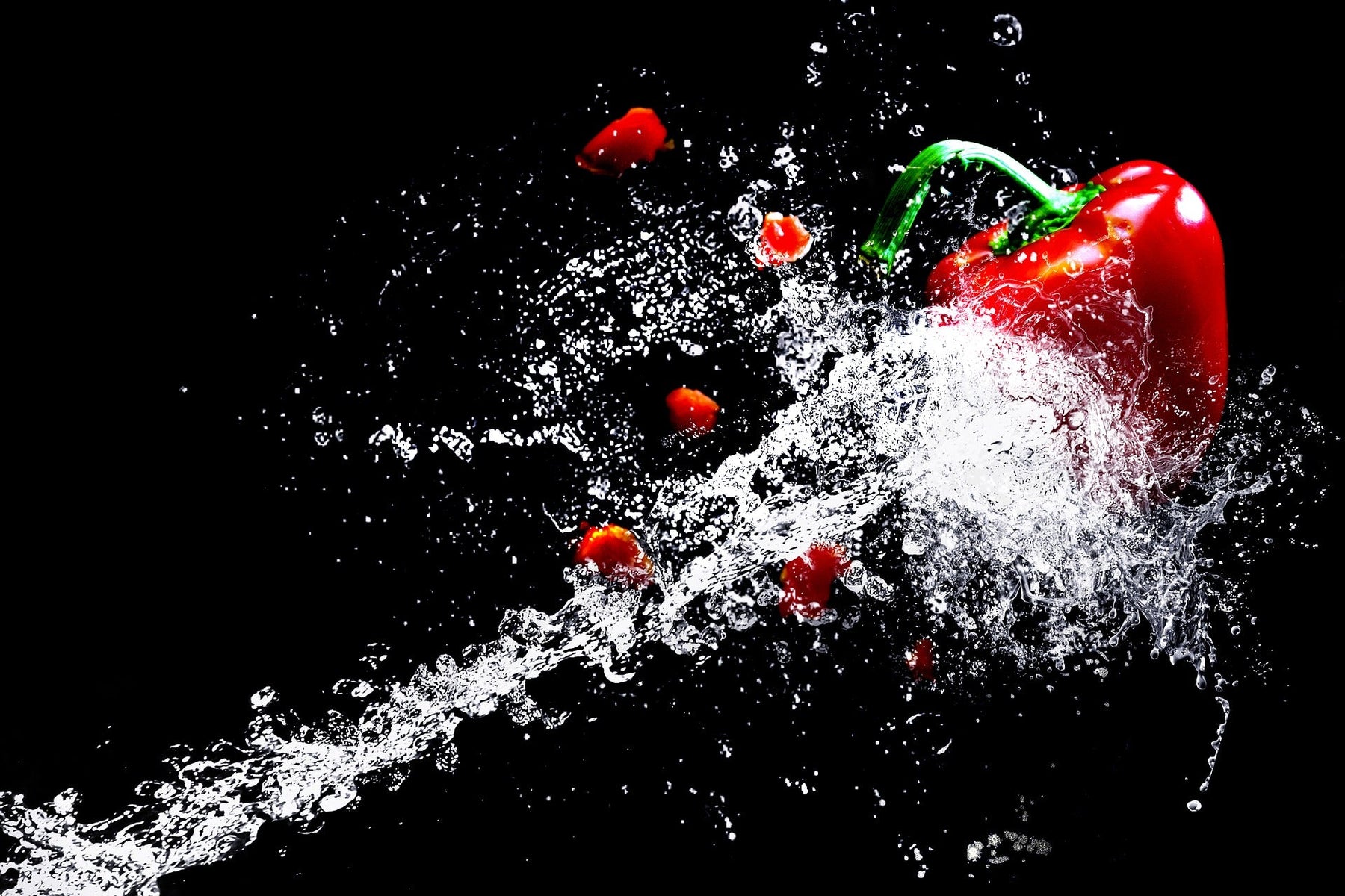 Red bell pepper being splashed by water on a black background