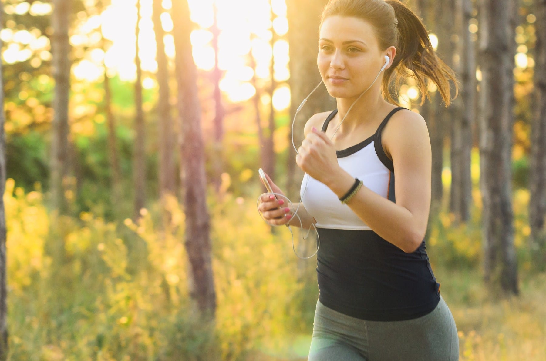 Woman listening to headphones running through woods