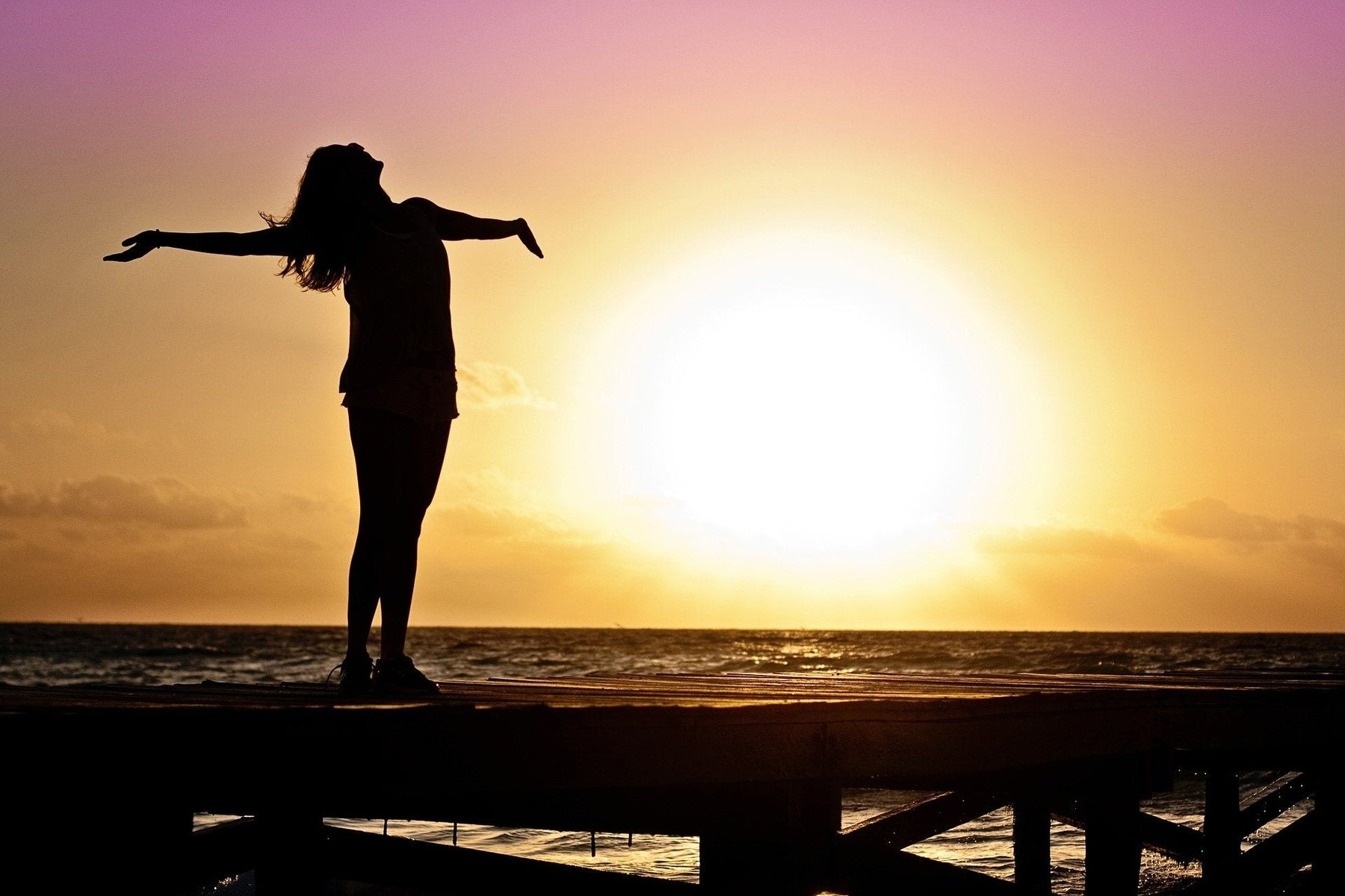 Woman with hands and head up overseeing a sunset over the ocean