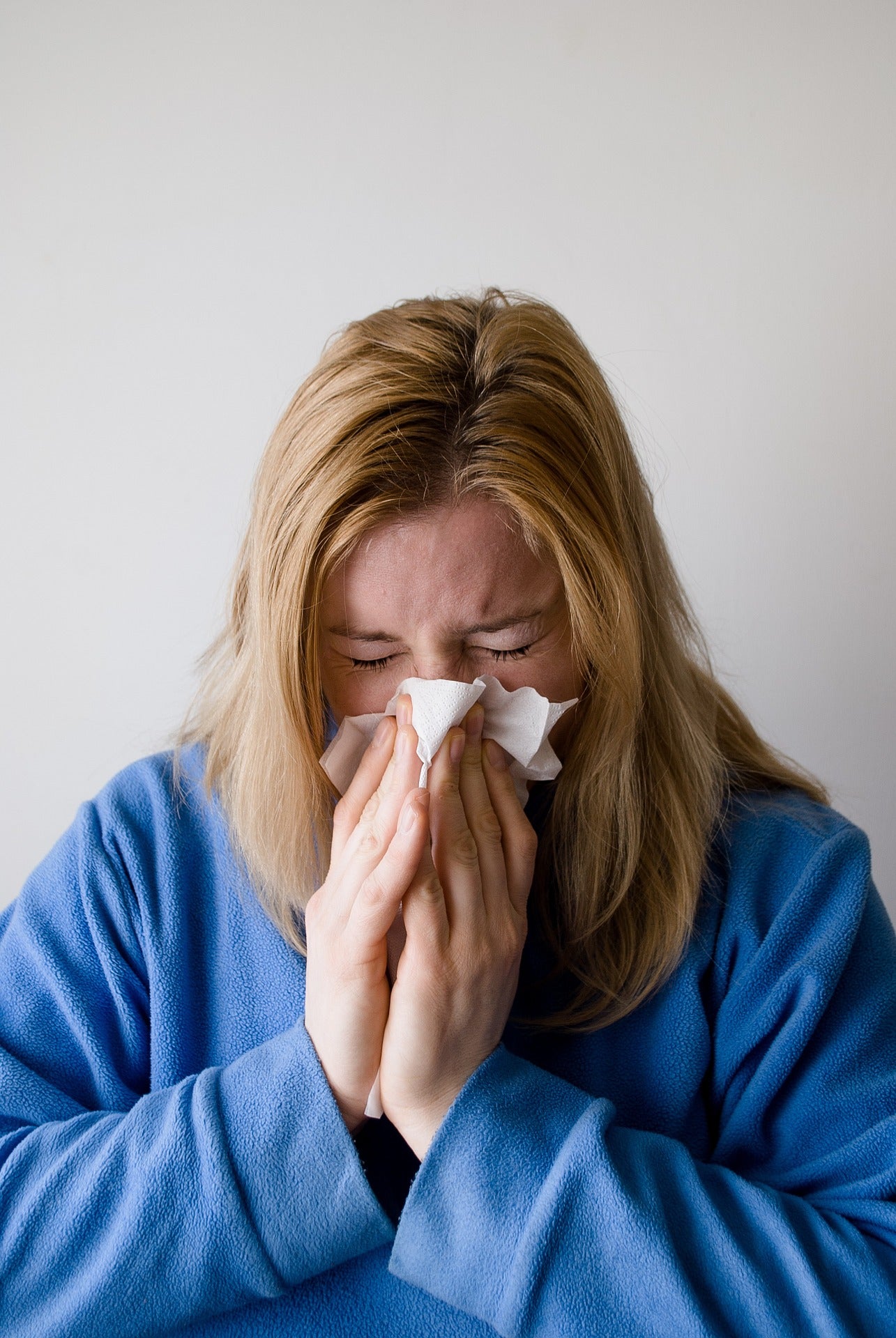 Woman dressed in blue blowing her nose