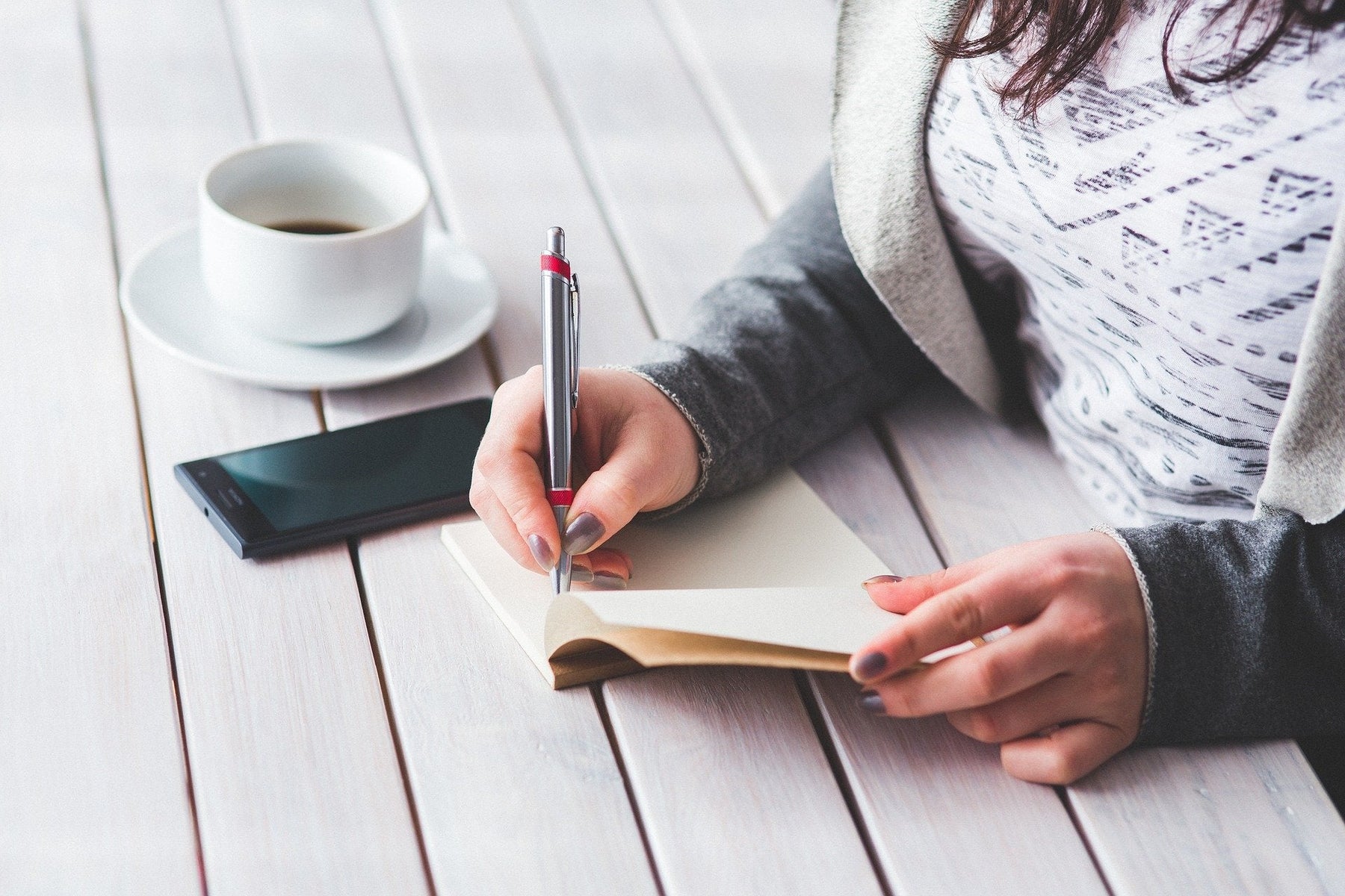 Woman taking notes on a notepad sitting next to her phone and a coffee