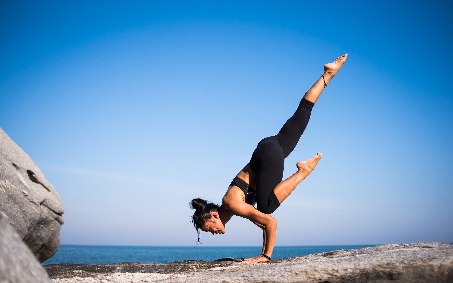 Woman doing yogo and standing in one hand next to a beach