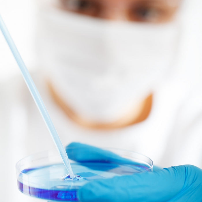 Man out of focus with blue gloves pouring liquid in a recipient