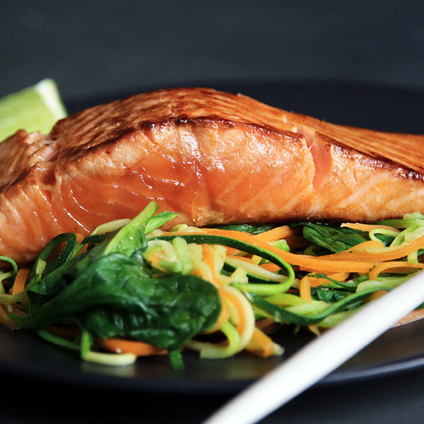 Grilled salmon with greens on a black plate sitting on a black table