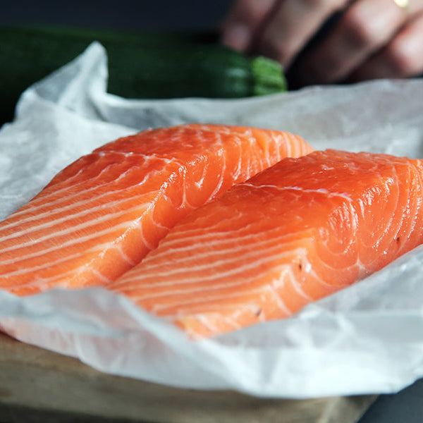 Salmon on a white sheet sitting on a black table with two carrots nearby