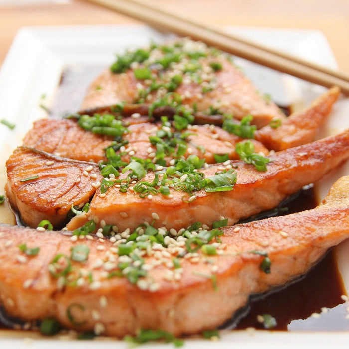 Salmon seasoned with greens sitting on a white plate along with chopsticks