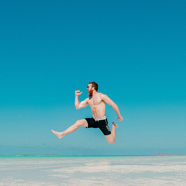 Shirtless man jumping in desert over a blue sky