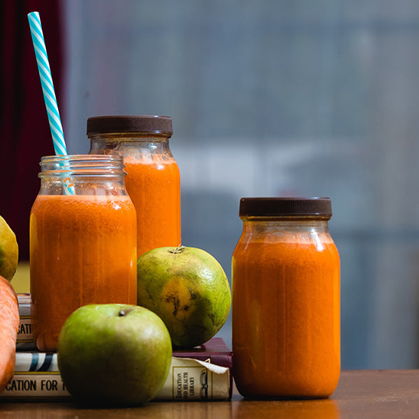 Healthy juices looking orange over five jars surrounded by fruits and vegetables