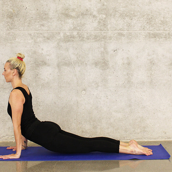 Blonde woman dressed in black doing yoga on a blue yoga mat
