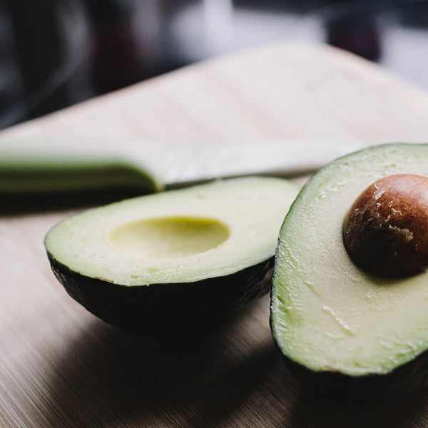 Avocado cut in half on a table along with a knife