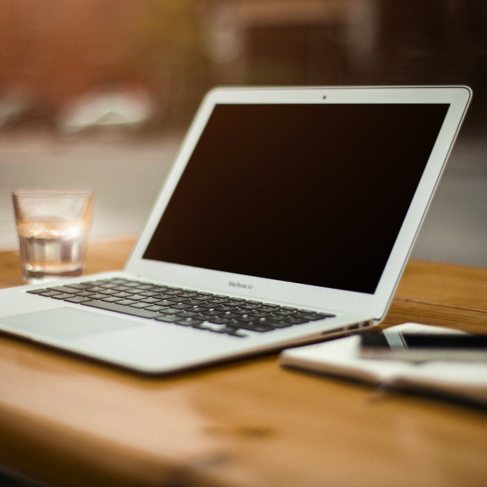 A laptop along with a glass of water and a notebook over a wooden desk
