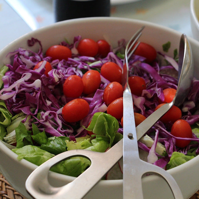 Salad with tomatoes sitting in a white bowl with a special salad claw