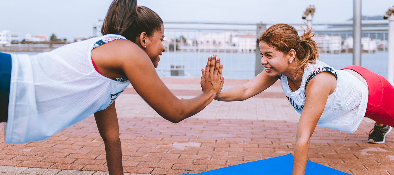 Two women in white doing push-ups, smiling and touching right hands