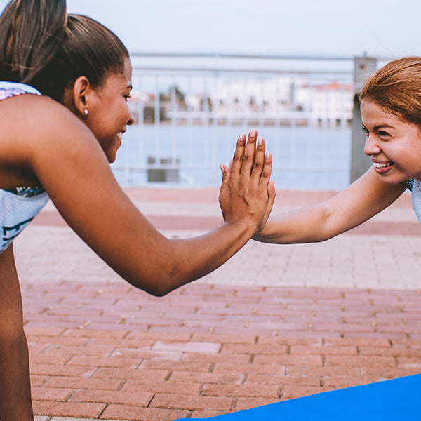 Two women in white doing push-ups, smiling and touching right hands