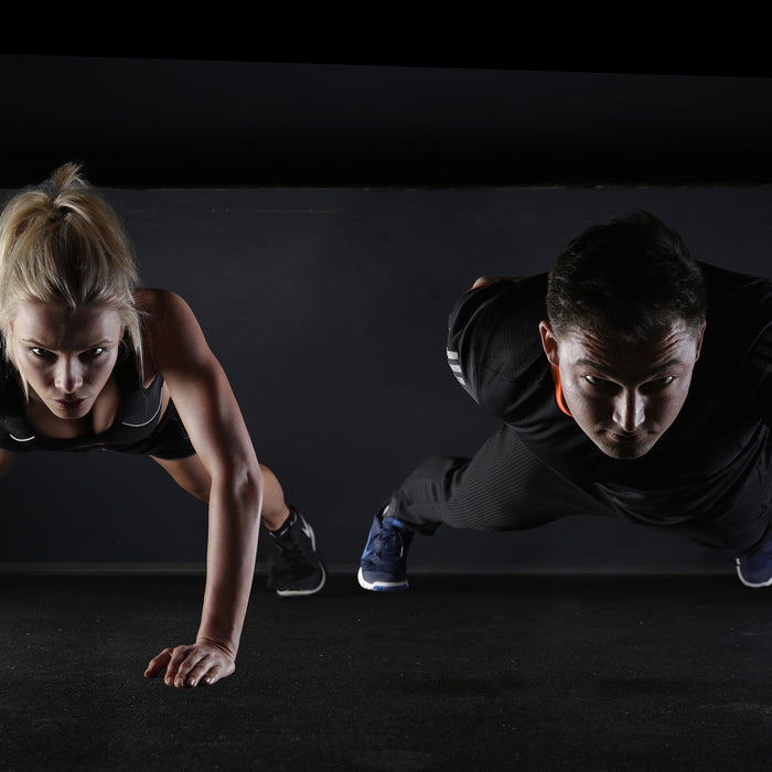 Woman and man doing a one-hand pushup in a black room