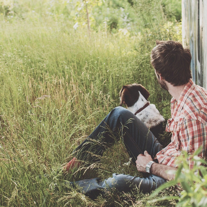 Man and a dog laying on the grass next to a white fence