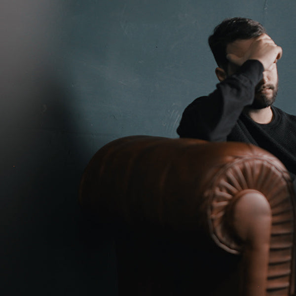 Man with headache laying on a brown lather sofa