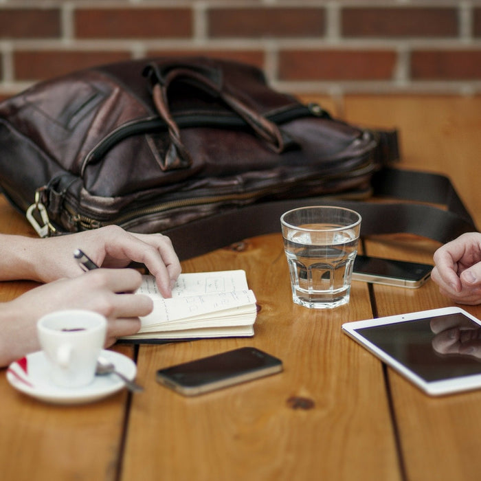 Two women taking notes over a wooden desk with a brown bag on the table