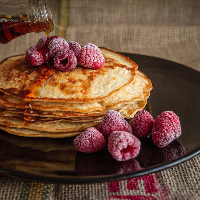 Syrup pouring over pancakes topped with raspberries