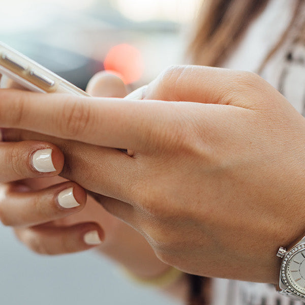 Woman dressed in white with white nails and a watch holding a smartphone