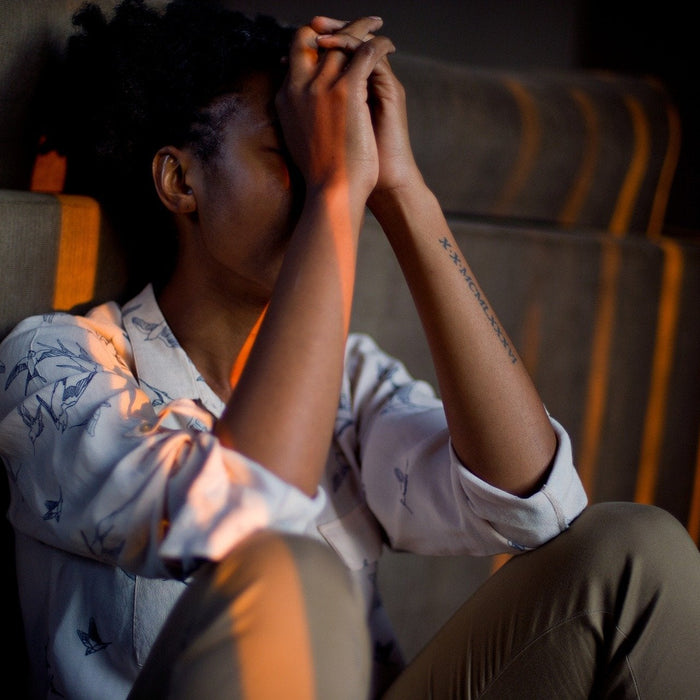 Sad woman sitting on a floor with her hands on her forehead