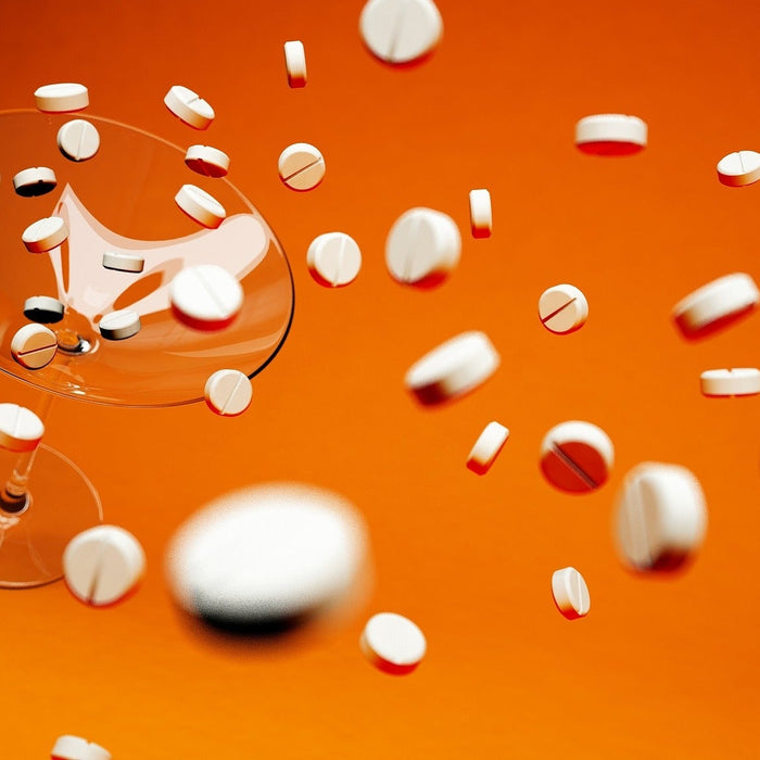 Pills falling over an empty glass sitting on an orange floor