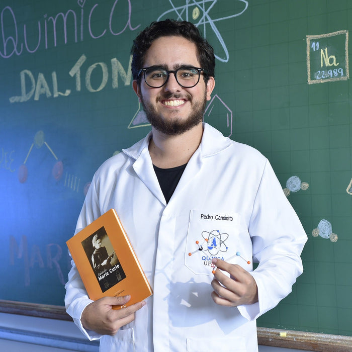 Smiling man dressed in white holding a book in front of a board