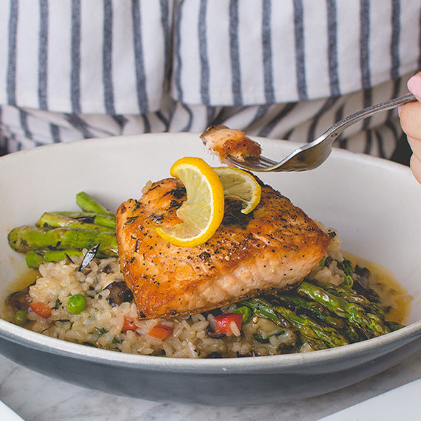 Woman eating salmon with rice and asparagus from a white plate