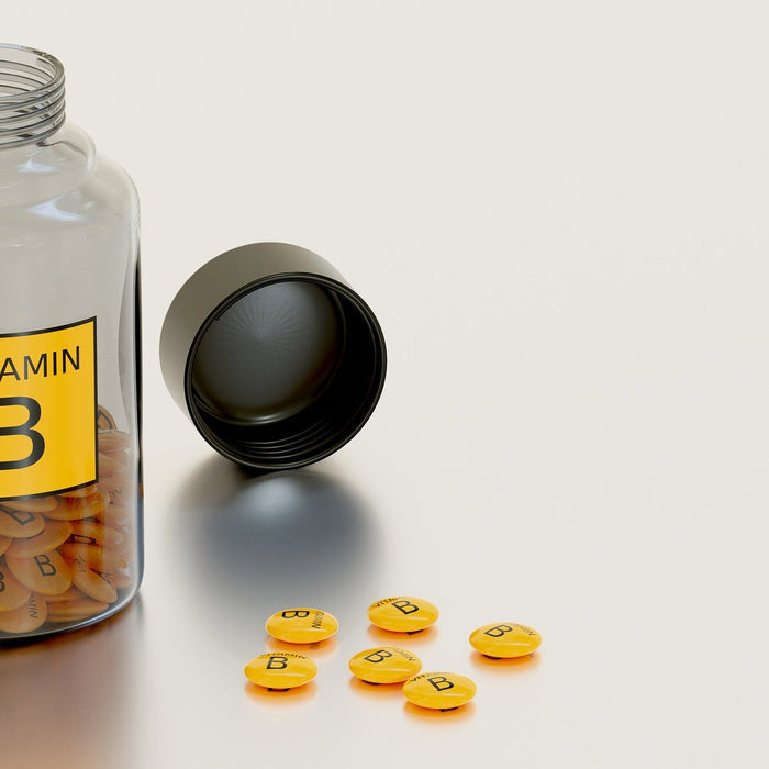 Glass bottle labeled Vitamin B half full with pills along some pills on the table